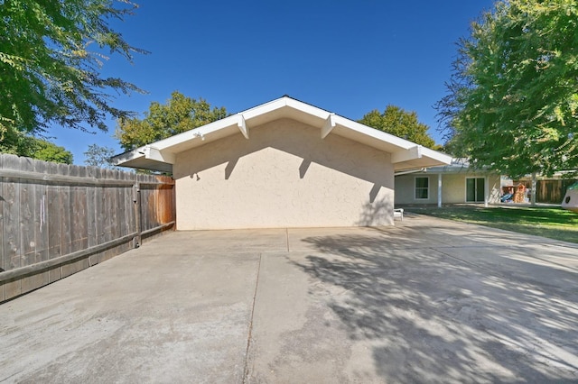 view of home's exterior with concrete driveway, a patio area, fence, and stucco siding