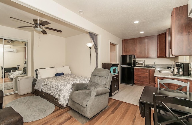 bedroom with a closet, black refrigerator, light wood-type flooring, a textured ceiling, and ceiling fan