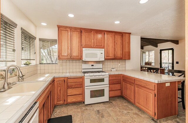 kitchen featuring kitchen peninsula, a healthy amount of sunlight, tile countertops, sink, and white appliances