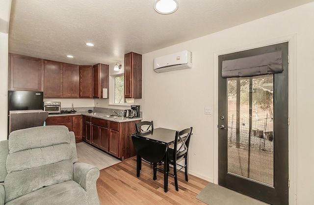 kitchen featuring a wall unit AC, black fridge, sink, light wood-type flooring, and a textured ceiling