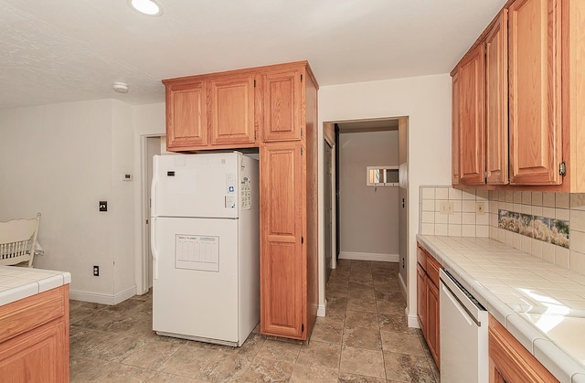 kitchen featuring tile countertops, white fridge, dishwashing machine, and tasteful backsplash