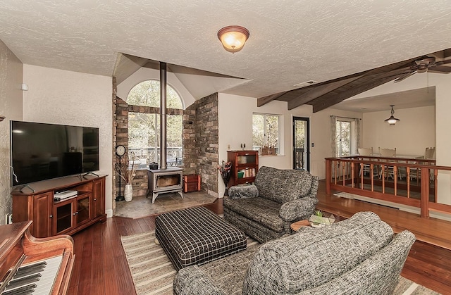 living room featuring vaulted ceiling with beams, a textured ceiling, a wood stove, and dark hardwood / wood-style flooring