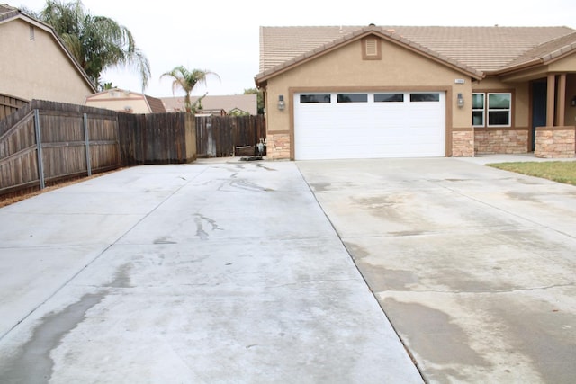 exterior space with stucco siding, fence, a garage, stone siding, and driveway