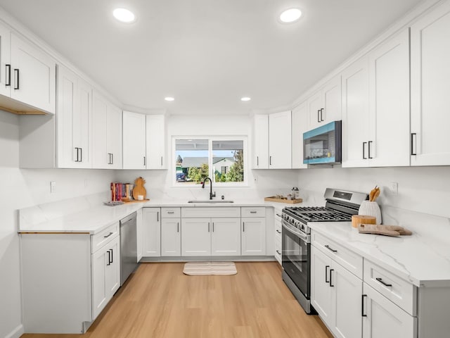 kitchen with light stone countertops, white cabinetry, sink, appliances with stainless steel finishes, and light wood-type flooring