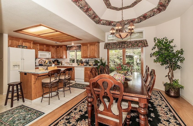 dining room featuring an inviting chandelier, light wood-type flooring, and a raised ceiling