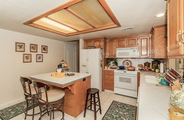 kitchen featuring white appliances, kitchen peninsula, a textured ceiling, and a kitchen bar