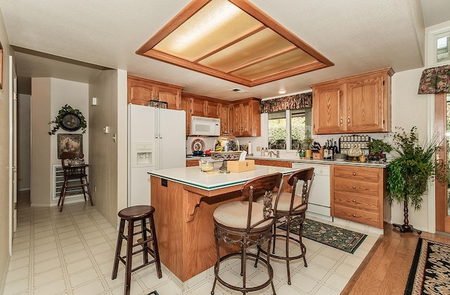 kitchen featuring a kitchen island, a breakfast bar, a textured ceiling, light wood-type flooring, and white appliances