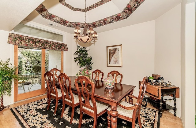 dining area featuring a notable chandelier, hardwood / wood-style flooring, and a raised ceiling