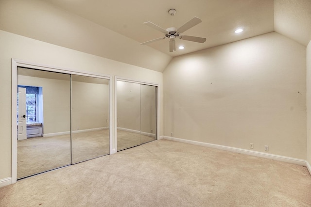 unfurnished bedroom with lofted ceiling, two closets, light colored carpet, and ceiling fan