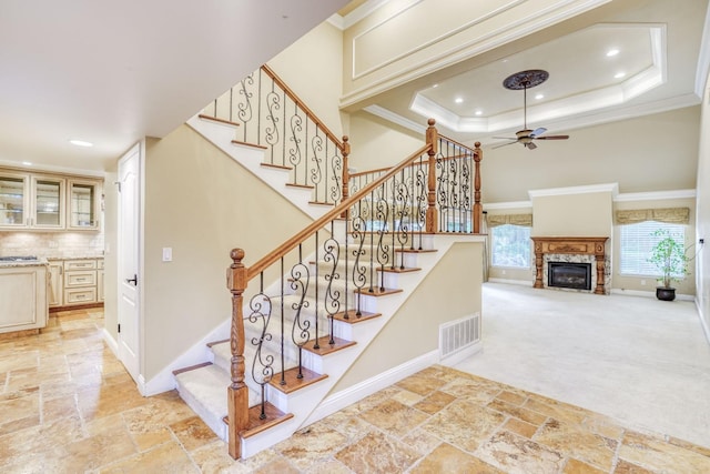 staircase featuring crown molding, a tray ceiling, carpet, and ceiling fan