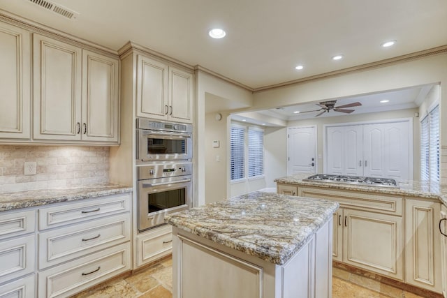 kitchen with a kitchen island, cream cabinets, ceiling fan, light stone counters, and tasteful backsplash