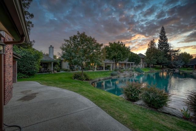 pool at dusk with a yard and a water view