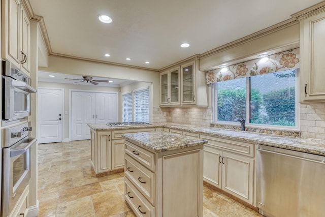 kitchen featuring tasteful backsplash, light stone countertops, cream cabinets, a kitchen island, and stainless steel appliances