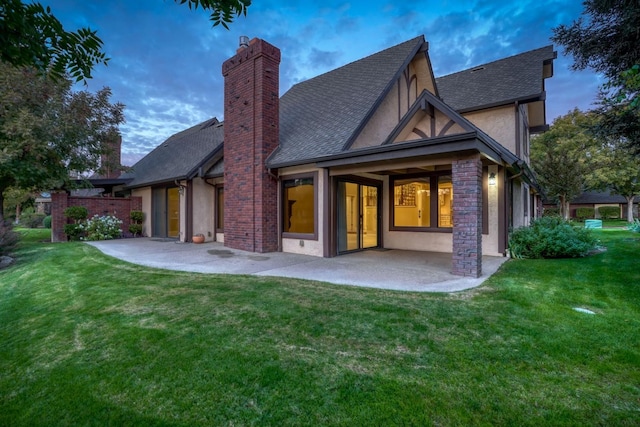 back house at dusk with a patio area and a lawn