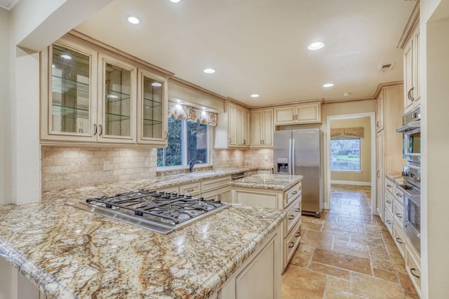 kitchen with tasteful backsplash, a kitchen island, appliances with stainless steel finishes, cream cabinetry, and light stone counters