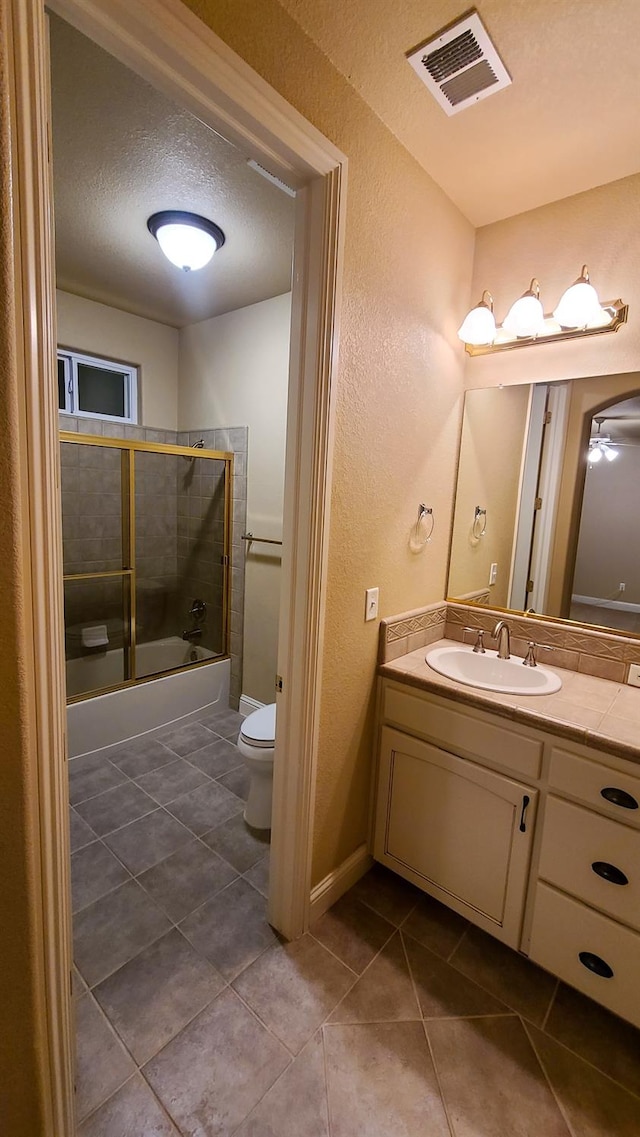 full bathroom featuring tile patterned floors, toilet, bath / shower combo with glass door, a textured ceiling, and vanity