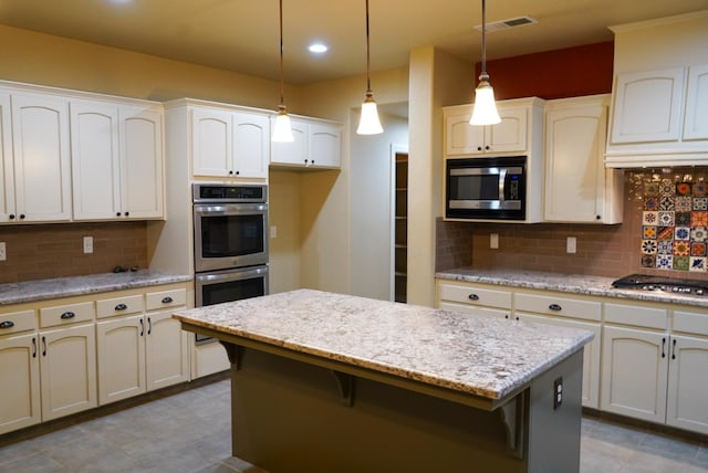 kitchen with light stone counters, appliances with stainless steel finishes, hanging light fixtures, a kitchen island, and decorative backsplash