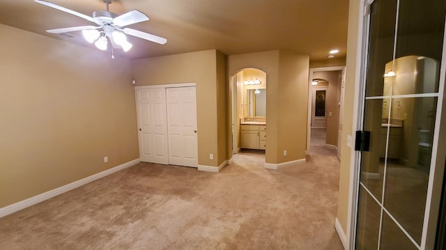 unfurnished bedroom featuring ensuite bath, light carpet, and ceiling fan