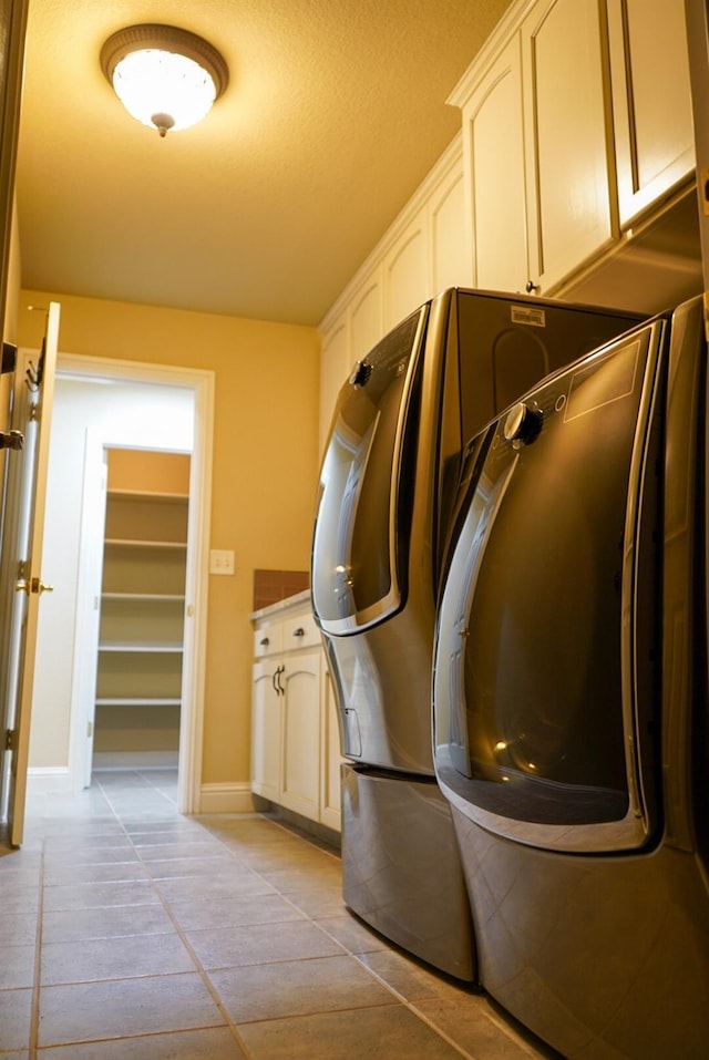 washroom with a textured ceiling, washing machine and clothes dryer, cabinets, and light tile patterned floors