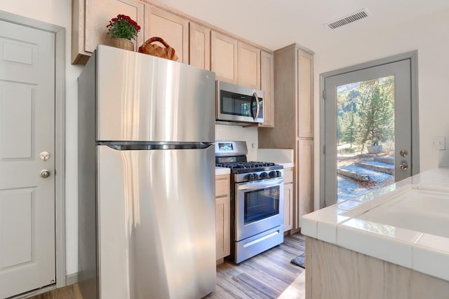 kitchen with tile countertops, light brown cabinetry, appliances with stainless steel finishes, and light wood-type flooring