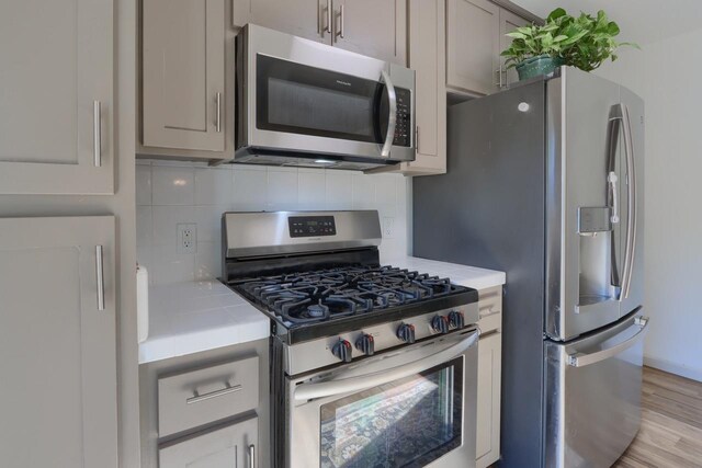 kitchen featuring light hardwood / wood-style floors, gray cabinetry, stainless steel appliances, and backsplash