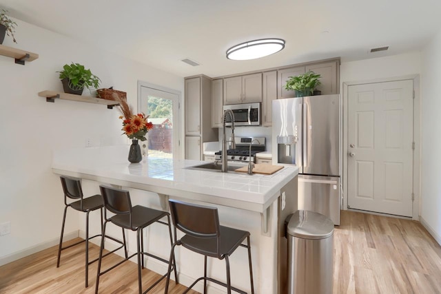 kitchen featuring gray cabinetry, light hardwood / wood-style flooring, kitchen peninsula, stainless steel appliances, and a breakfast bar