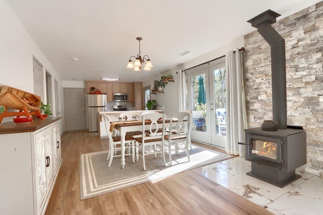 dining area with a wood stove, an inviting chandelier, and light wood-type flooring