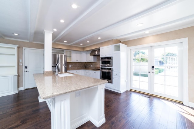 kitchen with a kitchen island with sink, sink, light stone countertops, white cabinetry, and tasteful backsplash