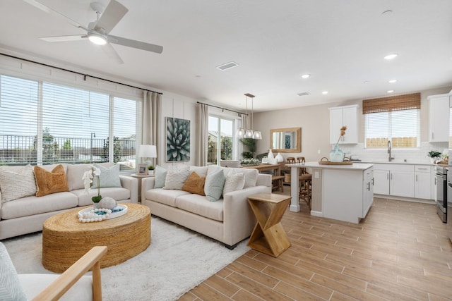 living room with ceiling fan with notable chandelier, sink, and light wood-type flooring