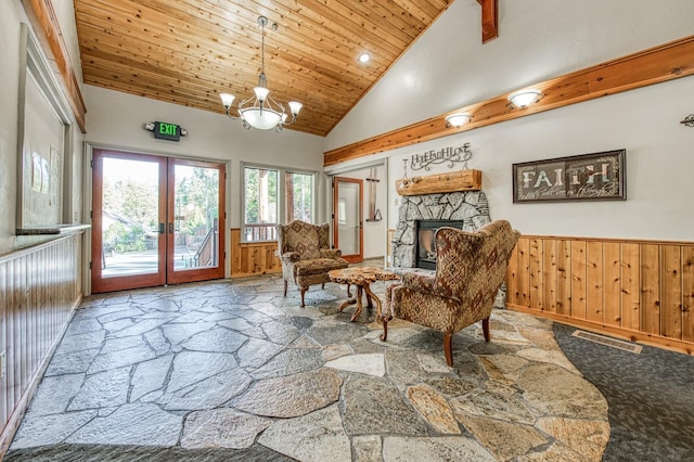 living area with wood walls, an inviting chandelier, high vaulted ceiling, a stone fireplace, and french doors