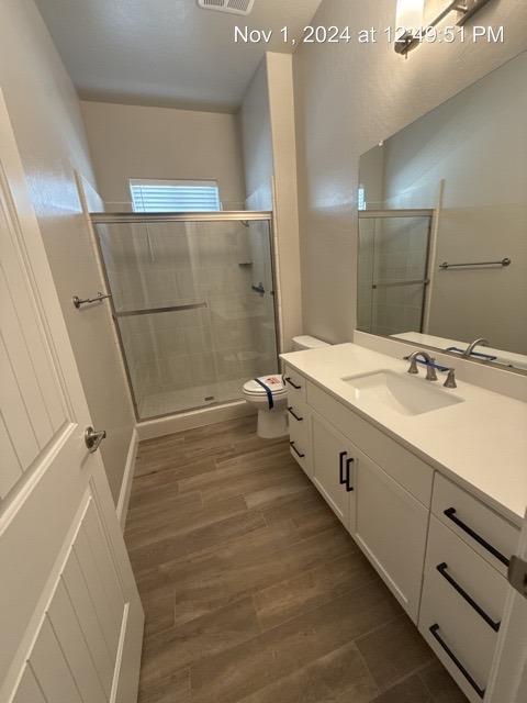 bathroom featuring hardwood / wood-style flooring, vanity, toilet, and a shower with shower door