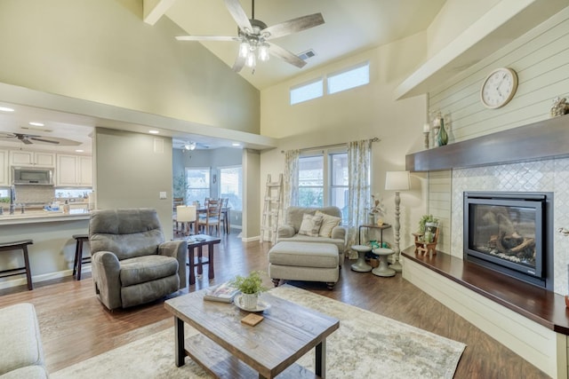 living room featuring high vaulted ceiling, wood-type flooring, a tile fireplace, and ceiling fan