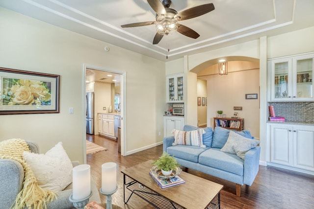 living room with dark wood-type flooring, ceiling fan, and a tray ceiling