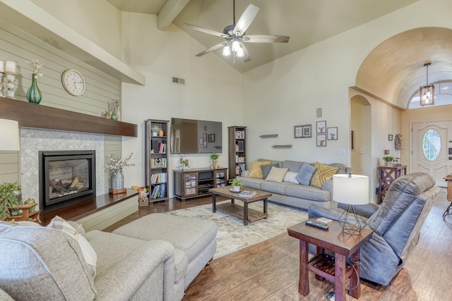 living room with beam ceiling, high vaulted ceiling, a tiled fireplace, hardwood / wood-style flooring, and ceiling fan