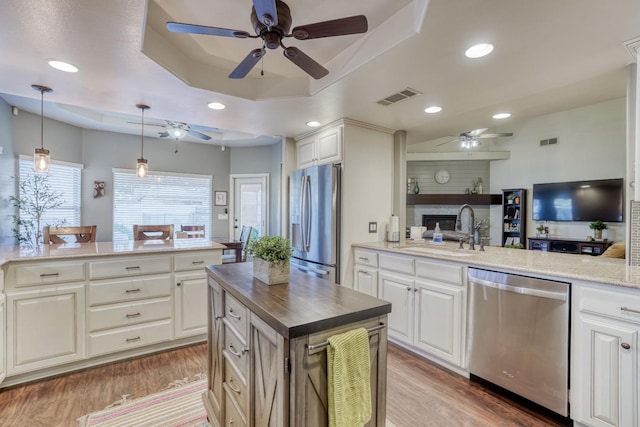 kitchen featuring light wood-type flooring, appliances with stainless steel finishes, decorative light fixtures, sink, and a tray ceiling