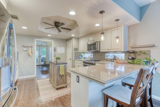 kitchen featuring light wood-type flooring, appliances with stainless steel finishes, decorative light fixtures, light stone countertops, and kitchen peninsula