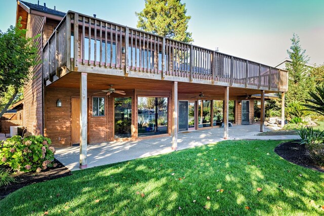 rear view of property featuring a lawn, ceiling fan, a wooden deck, and a patio