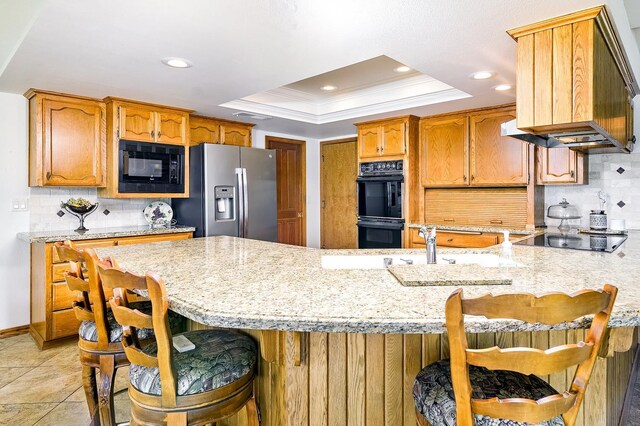 kitchen with a kitchen breakfast bar, tasteful backsplash, a tray ceiling, black appliances, and crown molding