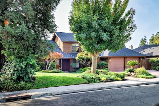 view of front of house featuring a front lawn, an attached garage, driveway, and a shingled roof