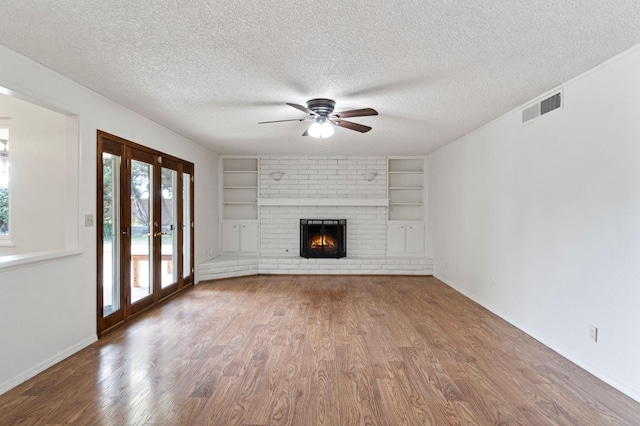 unfurnished living room with a brick fireplace, a textured ceiling, hardwood / wood-style flooring, and french doors