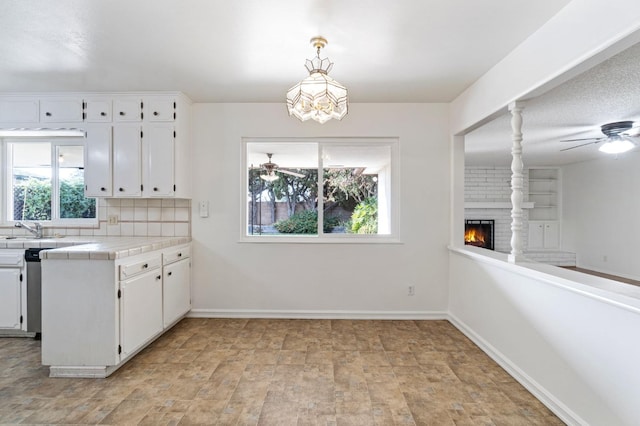 kitchen featuring pendant lighting, white cabinetry, a brick fireplace, tile countertops, and decorative backsplash