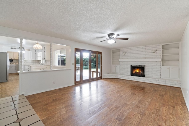 unfurnished living room with light wood-type flooring, ceiling fan, a textured ceiling, and a fireplace