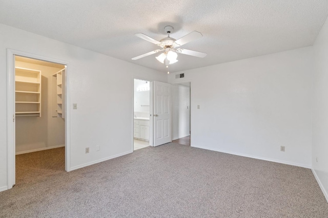 unfurnished bedroom featuring ensuite bath, a walk in closet, a closet, ceiling fan, and light colored carpet