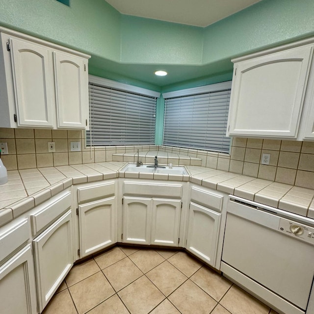 kitchen with white dishwasher, tile countertops, white cabinetry, and tasteful backsplash