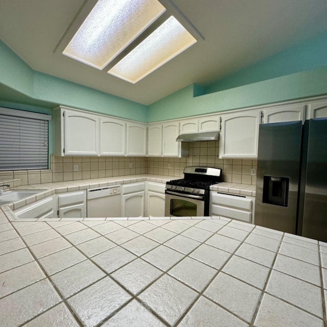 kitchen with tile counters, stainless steel appliances, lofted ceiling, and white cabinets