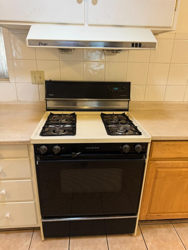 kitchen with light tile patterned flooring, range with gas stovetop, backsplash, and exhaust hood