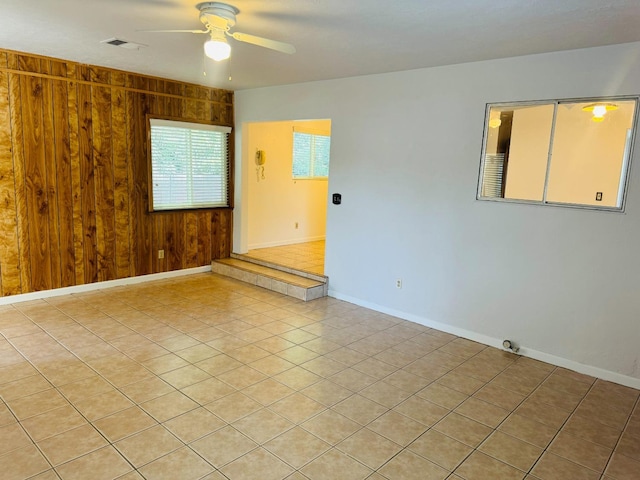 tiled empty room featuring wood walls and ceiling fan