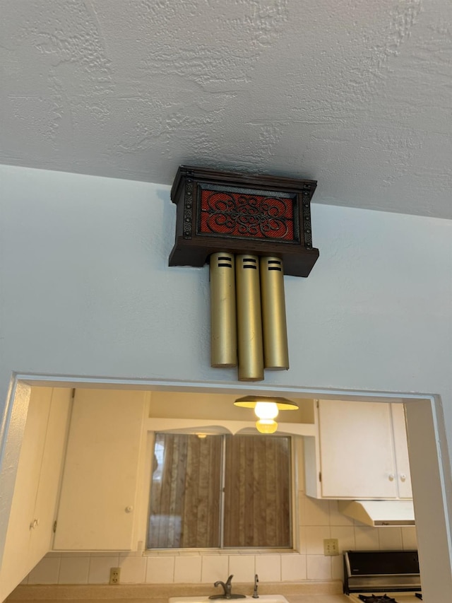 room details featuring sink, decorative backsplash, stove, and a textured ceiling