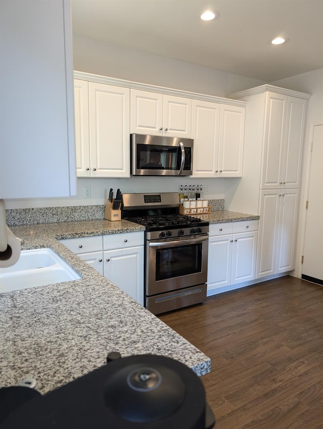 kitchen featuring stainless steel appliances, white cabinetry, dark hardwood / wood-style flooring, light stone countertops, and sink