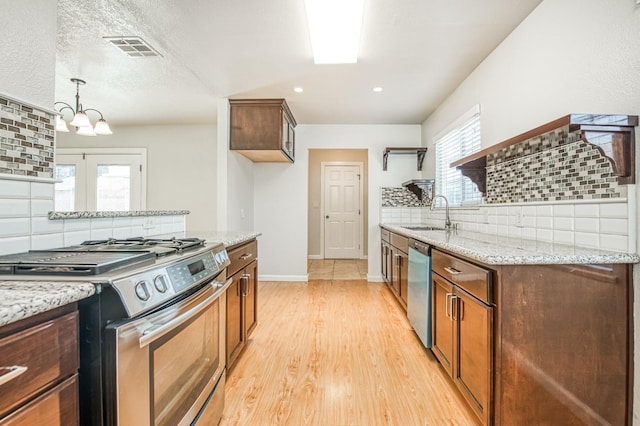 kitchen featuring sink, light stone counters, appliances with stainless steel finishes, tasteful backsplash, and light hardwood / wood-style flooring